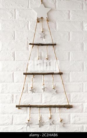 Elegante in legno albero di Natale in stile scandinavo contro lo sfondo bianco di un muro di mattoni. Semplice in stile minimalista del Natale e del nuovo anno home decor. Foto Stock