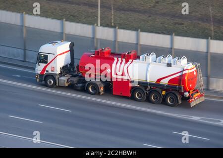 Grande e pesante cisterna con serbatoio in metallo lucido zoppo guida su autostrada città, vista aerea laterale Foto Stock