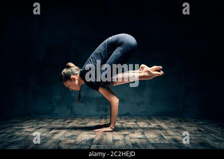 Giovane donna che pratica yoga facendo braccio gru posare asana in camera oscura Foto Stock