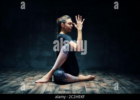 Giovane bella donna che fa yoga asana mezzo signore dei pesci posa in camera oscura Foto Stock