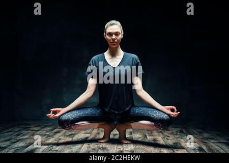 Giovane bella donna che fa yoga asana tipoe posa prapadasana variazione in camera oscura Foto Stock