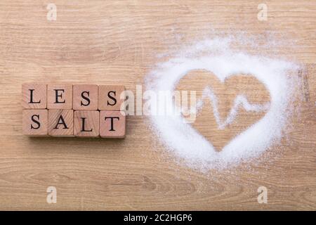 Meno sale vicino a forma di cuore con il battito del cuore sulla scrivania in legno Foto Stock