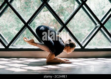 Giovane bella donna che fa yoga asana baby corvo posa su sfondo triangolare finestra Foto Stock