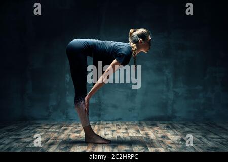 Giovane bella donna che fa yoga asana mezza sedia posa su camera oscura. Foto Stock