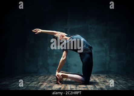 Giovane donna attraente che pratica yoga facendo mezzo cammello posa in camera oscura Foto Stock