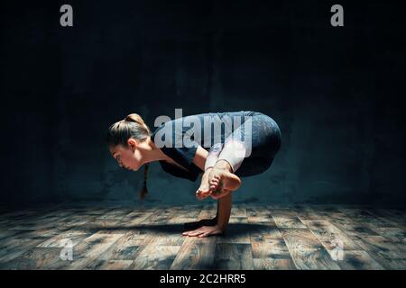 Giovane donna attraente che pratica yoga facendo posa gru laterale in camera oscura Foto Stock