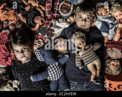 Foto di creepy giovani bambini sul pavimento circondato da vecchi bambole per tema di Halloween. Foto Stock