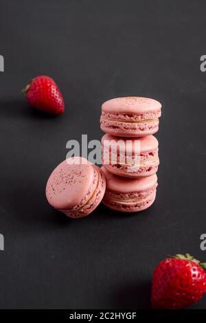Macaron di fragole su sfondo scuro. I macaron sono delicati dolci francesi fatti di biscotti rotondi di meringa e di un ripieno dolce nel centro. Foto Stock