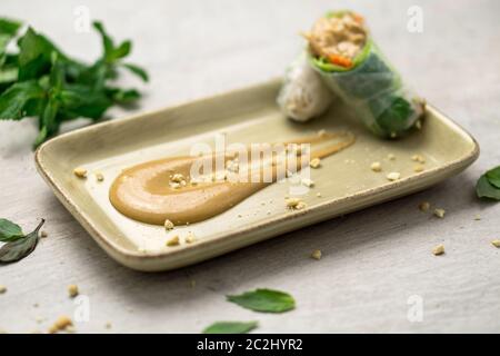 Deliziosa salsa cremosa di burro di arachidi su un piatto con croccanti briciole di arachidi e involtini di primavera vietnamiti sul lato. La salsa al burro di arachidi è morbida Foto Stock