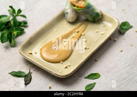 Deliziosa salsa cremosa di burro di arachidi su un piatto con croccanti briciole di arachidi e involtini di primavera vietnamiti sul lato. La salsa al burro di arachidi è morbida Foto Stock