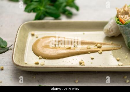 Deliziosa salsa cremosa di burro di arachidi su un piatto con croccanti briciole di arachidi e involtini di primavera vietnamiti sul lato. La salsa al burro di arachidi è morbida Foto Stock