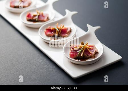 Tataki di tonno è un piatto giapponese che consiste di bistecca di tonno scottata brevemente in fette sottili. Servito come antipasto con salsa al brandy su sfondo scuro. Foto Stock