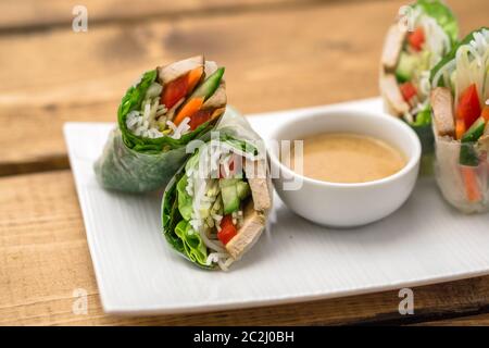 Panini freschi di primavera vietnamiti, ottimi come un antipasto sano con salsa al burro di arachidi per tuffarsi. La piastra è posta su uno sfondo di legno. Foto Stock