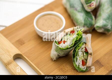 Panini estivi vietnamiti freschi, ottimi come un antipasto sano con salsa al burro di arachidi per tuffarsi. Il cibo è posto su un tagliere di legno. Foto Stock