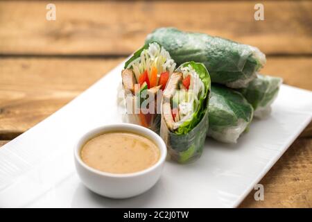 Panini freschi di primavera vietnamiti, ottimi come un antipasto sano con salsa al burro di arachidi per tuffarsi. La piastra è posta su uno sfondo di legno. Foto Stock
