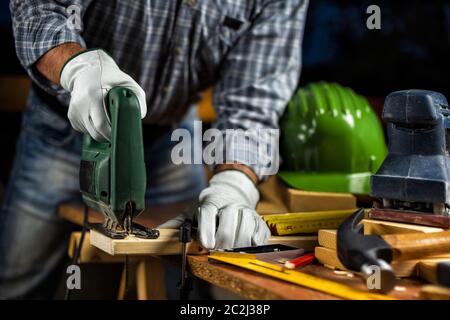 Adulto falegname artigiano protettivo indossa i guanti di cuoio, con sega elettrica lavorando sul taglio di un tavolo di legno. Edilizia Lavori di casa do it Foto Stock