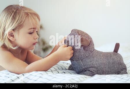 Ritratto di un piccolo grazioso baby boy divertendosi con il suo piccolo amico, giocattolo morbido doggy, con il piacere di trascorrere del tempo a casa e prepararsi al pan Foto Stock