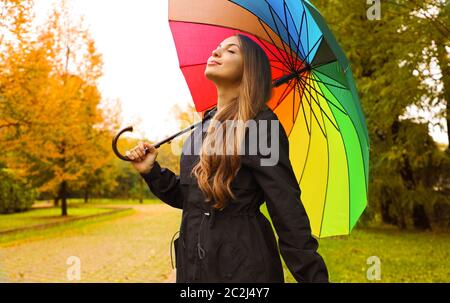 Ritratto di una donna felice indossando un impermeabile sotto un ombrello respirazione nel parco della città sul giorno di pioggia. Foto Stock