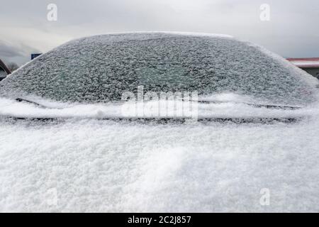 Una chiusura di un'auto con un parabrezza e un cofano innevati. La vettura non è identificabile. Cielo sovrastante. Foto Stock