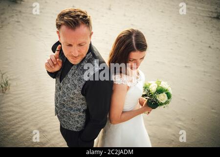 Vista della vicina sposa e dello sposo che si erigono sulla spiaggia di sabbia e guardano nella stessa direzione. Sposi alla luce della sera. Concetto di giorno di nozze. Foto Stock