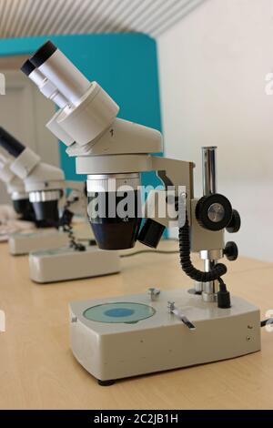 Microscopio binoculare con supporto utilizzato per il college di insegnamento o il lavoro di laboratorio su un marrone chiaro tavolo. Foto Stock