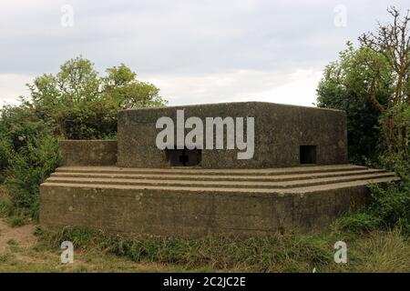 Un FW3/22 tipo guerra mondiale due scatola di pillole sulla costa orientale dell'Inghilterra con due lacune e circondato da alberi e arbusti con un grigio blu cielo. Foto Stock