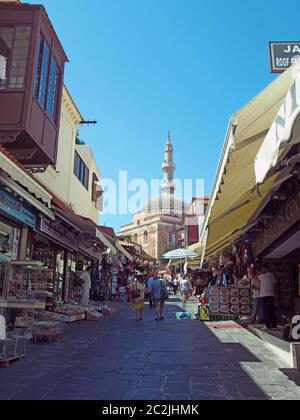 i turisti camminano lungo una strada fiancheggiata da negozi e caffè vicino alla vecchia moschea suleiman nella città di rodi Foto Stock