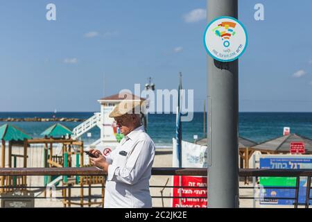 Tel Aviv/Israel-10/10/18: Un anziano che sta vicino al cartello Free WI-Fi zone, cercando di accedere online tramite il suo smartphone sul lungomare di Tel Aviv Foto Stock
