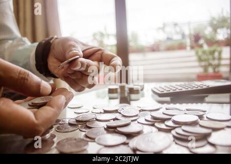 Immagine ritagliata di imprenditore contare monete utilizzando la calcolatrice a scrivania in ufficio. Commercianti lato contare monete. Finanza aziendale e risparmio Inves Foto Stock