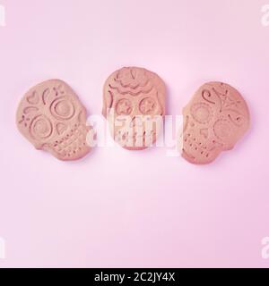 Il concetto di giorno dei morti. Tre biscotti fatti in casa allo zenzero a forma di teschi, sopra un quadrato sparato su uno sfondo rosa con co Foto Stock