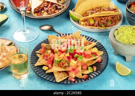 Cibo messicano con nachos davanti e conchiglie di taco con carne di maiale tirata, burritos, guacamole e altri piatti, con tequila e lime Foto Stock
