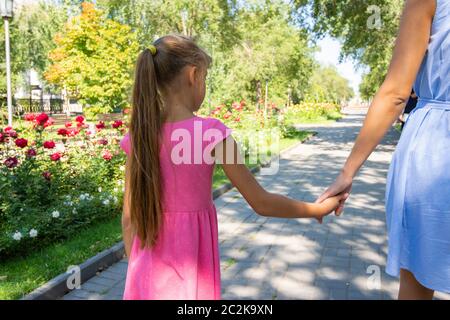 Una ragazza cammina lungo il vicolo e trattiene la mamma mano Foto Stock