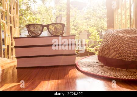 Vista laterale anteriore del libro e occhiali da sole con un cappello di paglia. Estate vacanze la nozione di sfondo. Foto Stock