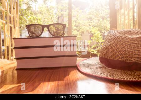 Vista laterale anteriore del libro e occhiali da sole con un cappello di paglia. Estate vacanze la nozione di sfondo. Foto Stock