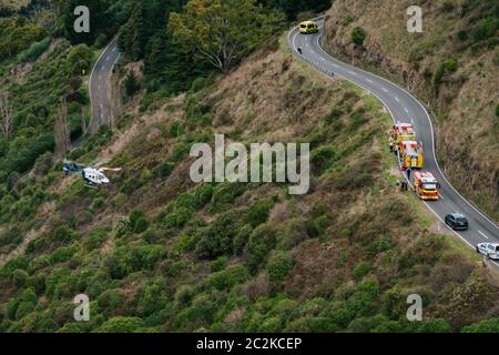 Un elicottero di soccorso BK117 / H145 recupera l'attrezzatura dagli equipaggi che liberano un conducente da un veicolo che è caduto su una ripida collina coperta da scrub Foto Stock