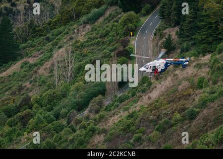 Un elicottero di salvataggio BK117 / H145 recupera il conducente di un veicolo che ha lasciato la strada e cadde su una ripida collina coperta di cespugli a Christchurch, Nuova Zelanda Foto Stock