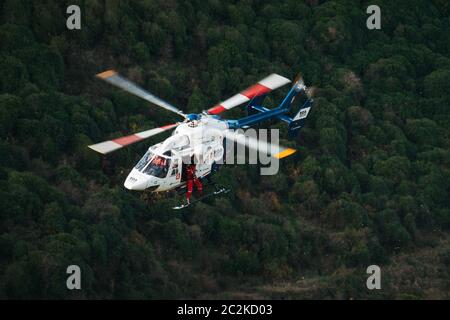 Un elicottero di salvataggio BK117 della West Coast Air Rescue Trust di Canterbury abbassa le attrezzature sul sito di un'auto che cadde su una ripida banca in Nuova Zelanda Foto Stock