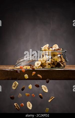 Frutta disidratata in aprire il vasetto di vetro sul tavolo di legno con frutti che ricade verso il basso Foto Stock