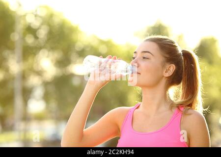 Happy runner acqua potabile da una bottiglia in piedi in un parco dopo lo sport Foto Stock