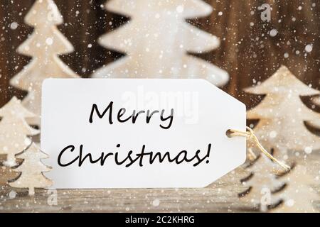 Etichetta con testo in inglese Buon Natale. Legno bianco albero di Natale come decorazione. In legno marrone dello sfondo con la neve Foto Stock