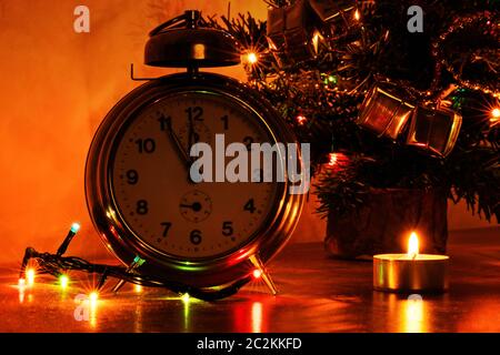 Quasi il tempo per la celebrazione. Un'immagine ravvicinata di un vecchio orologio con candele, luci di Natale e albero di Natale in background. Foto Stock