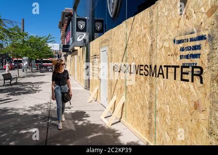 Giovane donna che cammina per le strade di Toronto guardando a bordo su storefront con Black Lives messaggio materia sostegno movimento contro l'ingiustizia. Foto Stock