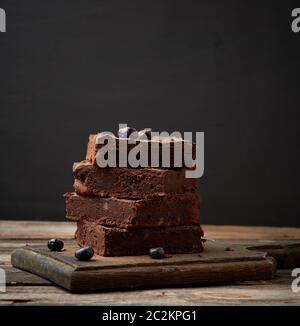 Pila di cotto quadrato fette di brownie torta al cioccolato con noci su una superficie di legno. Cuocere cibi fatti in casa. Pasticceria al cioccolato. Farina dolce casereccio Foto Stock