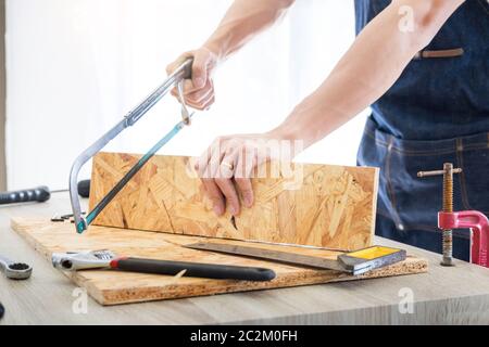 Carpenter operando con cautela guardando i piani di lavoro in falegnameria. Egli è imprenditore di successo al suo posto di lavoro. martellare un chiodo supporta sulla build Foto Stock