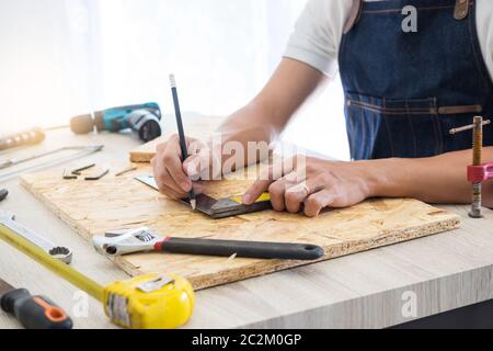 Carpenter operando con cautela guardando i piani di lavoro in falegnameria. Egli è imprenditore di successo al suo posto di lavoro. martellare un chiodo supporta sulla build Foto Stock