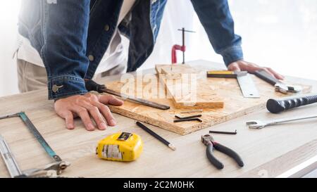 Carpenter operando con cautela guardando i piani di lavoro in falegnameria. Egli è imprenditore di successo al suo posto di lavoro. martellare un chiodo supporta sulla build Foto Stock