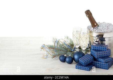 Ancora vita con bottiglia di champagne in piedi in secchio con ghiaccio, flauti di champagne, scatole regalo, ramo di abete, decorazione di Natale su tavolo di legno su bianco Foto Stock