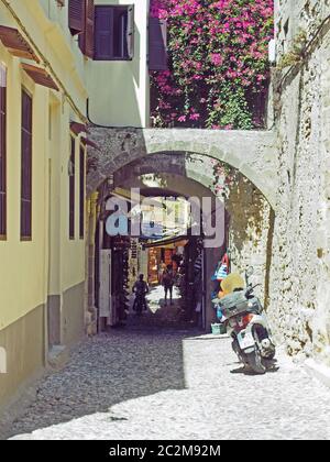 la gente cammina attraverso negozi e archi antichi in una strada stretta nella città di rodi in piena luce del sole Foto Stock