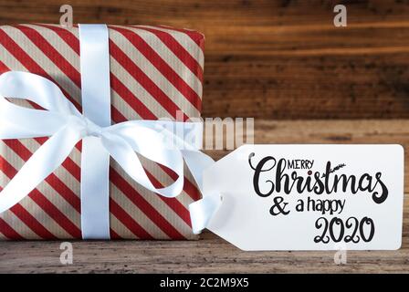 Un regalo di Natale con etichetta con la calligrafia inglese Buon Natale e un felice 2020. La carta di avvolgimento di un arco Foto Stock