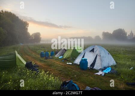 Tende su un campo in nebbia di mattina presto, l'alba drammatica bagliore sull'orizzonte Foto Stock
